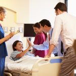 Medical Team Meeting Around Female Patient In Hospital Room