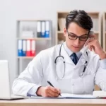 A Doctor Sitting At A Desk Writing On A Paper